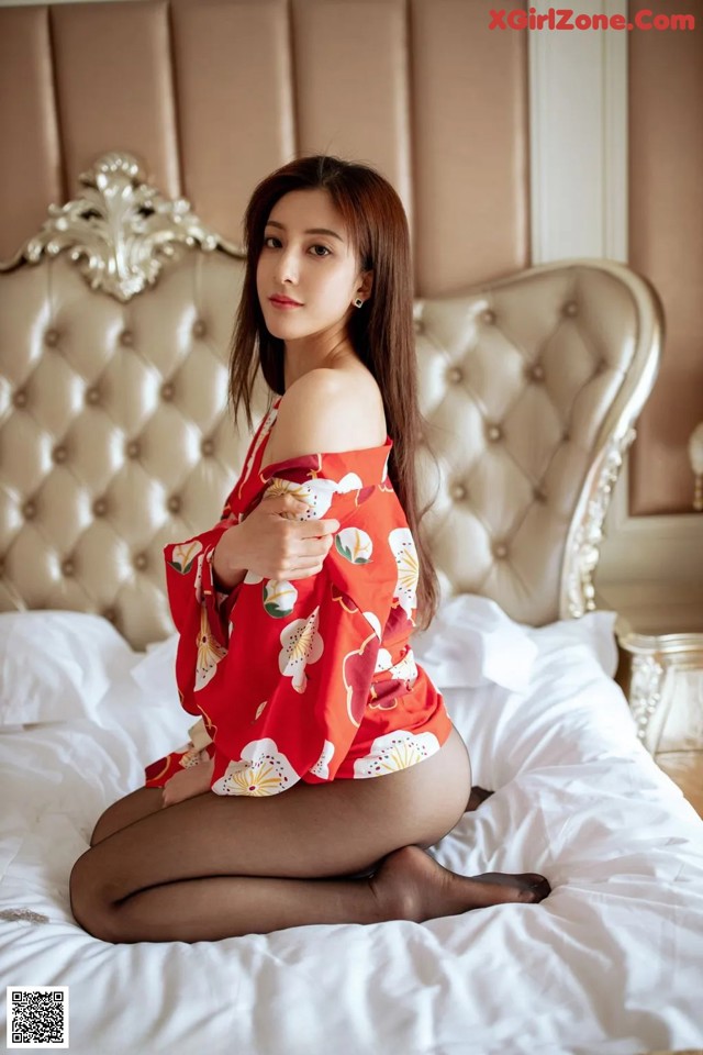 A woman in a red dress sitting on a bed.