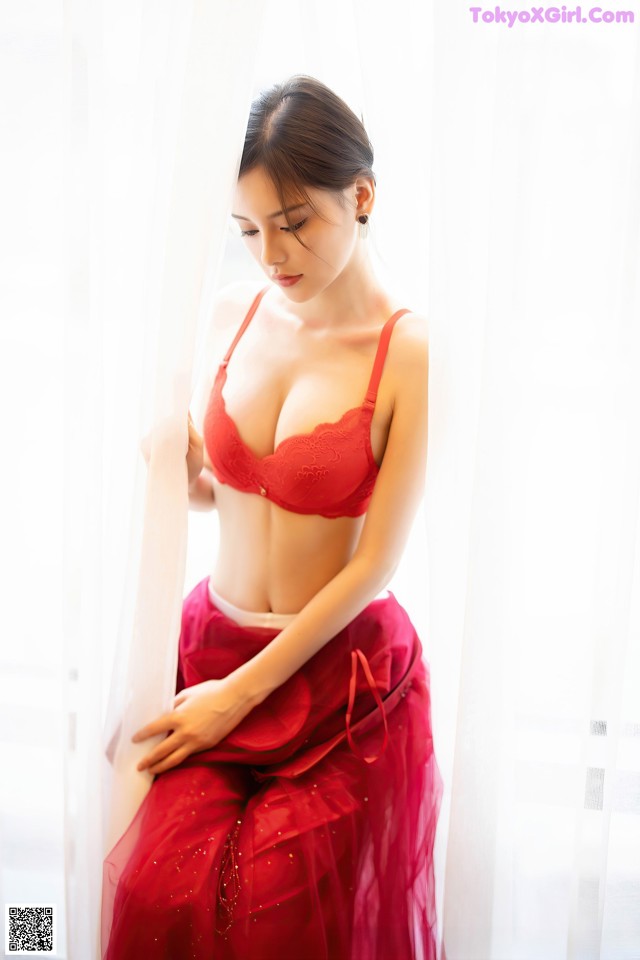 A woman in a red lingerie leaning against a curtain.