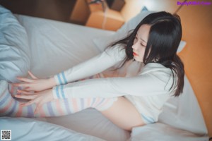 A woman sitting on a bed in a white shirt and striped socks.