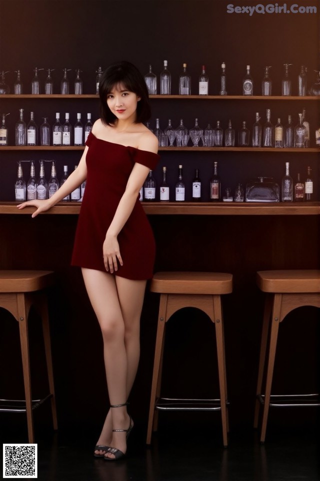 A woman in a red dress standing in front of a bar.