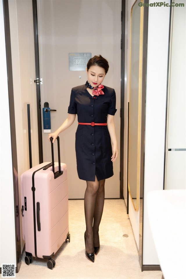 A woman in a blue dress holding a pink suitcase.