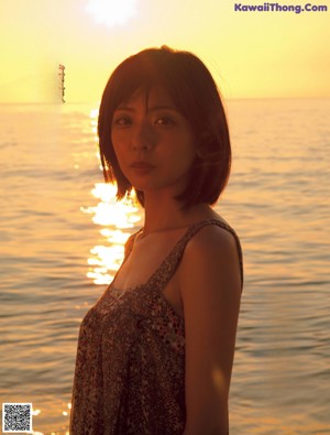 A woman in a black dress leaning against a rock.