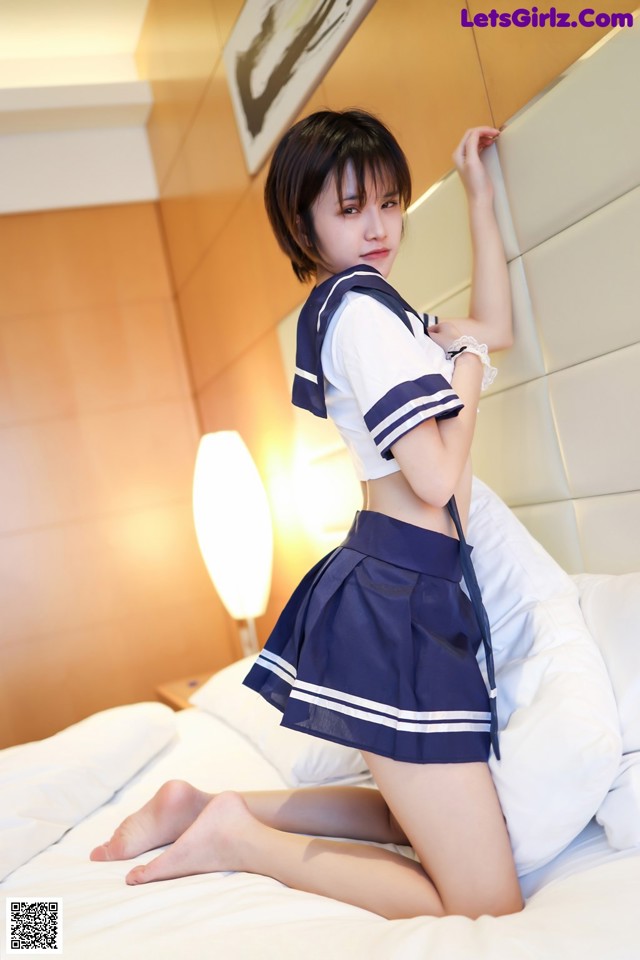 A woman in a school uniform is posing on a bed.