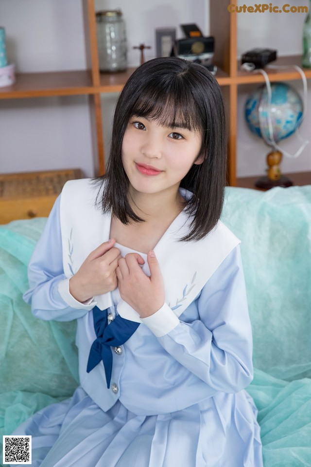 A woman in a blue dress sitting on a bed.