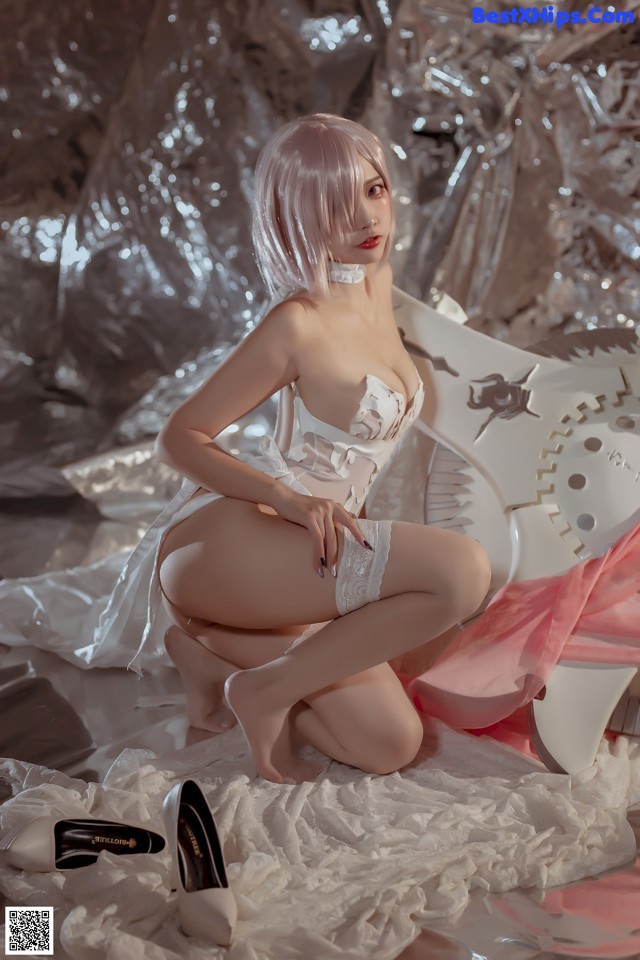 A woman in a white corset and stockings sitting on a bed.