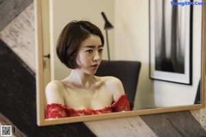 A woman in a red dress sitting at a desk in front of a mirror.
