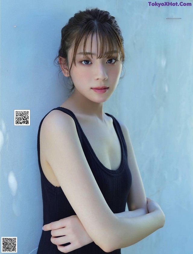 A woman in a black tank top leaning against a wall.