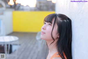 A young girl leaning against a white wall.