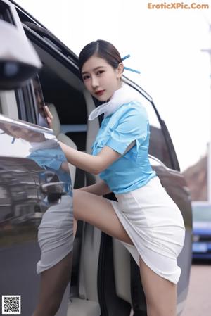 A woman in a blue shirt and white skirt getting out of a car.