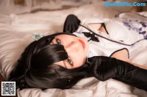 A woman in a maid outfit sitting on a bed.