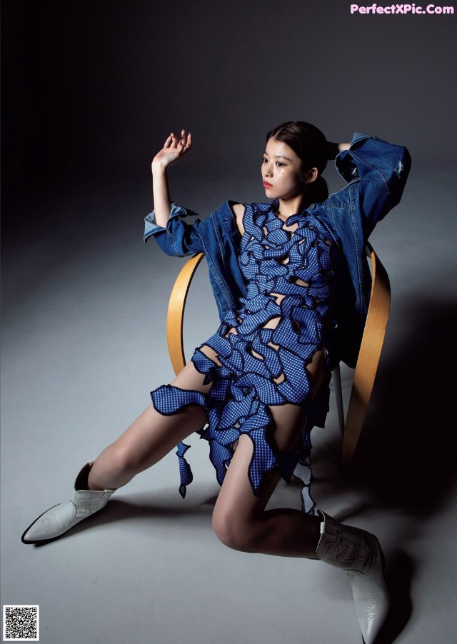 A woman sitting on a chair wearing a blue dress and a denim jacket.