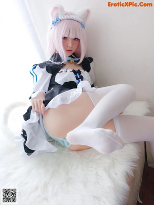 A woman in a maid outfit sitting on a bed.