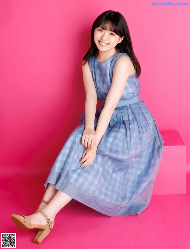 A woman in a blue dress sitting on a pink cube.