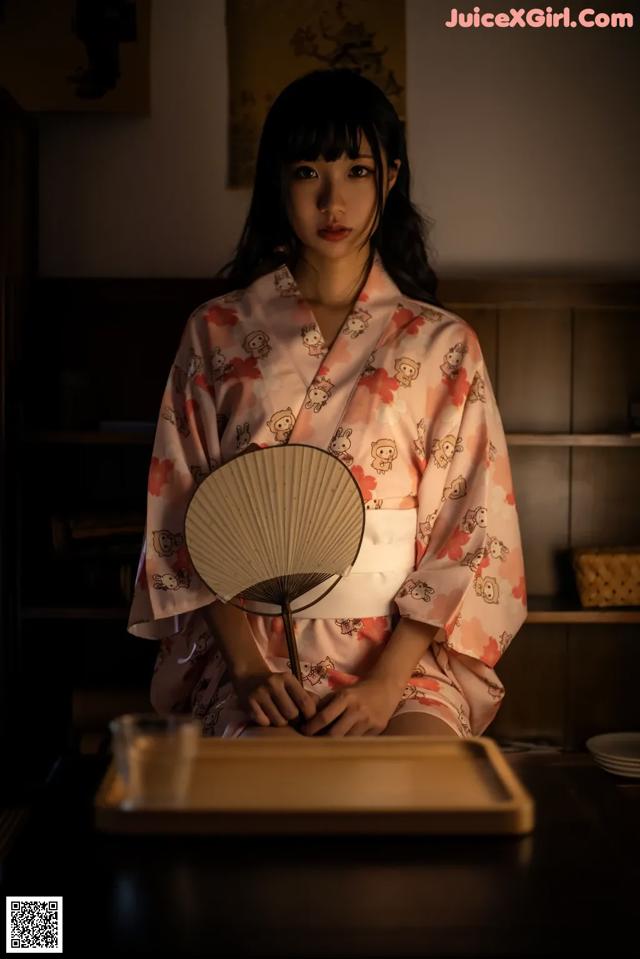 A woman in a kimono sitting at a table with a fan.