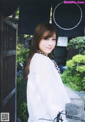 A woman in a white kimono standing in front of a gate.