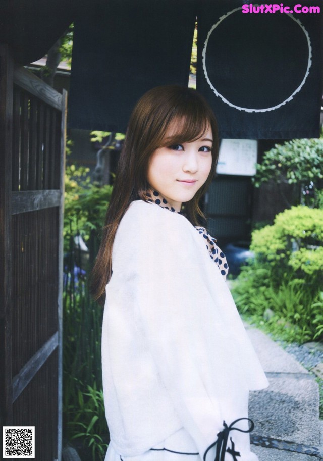 A woman in a white kimono standing in front of a gate.