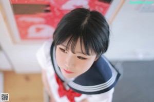 A woman in a school uniform sitting on a bed.