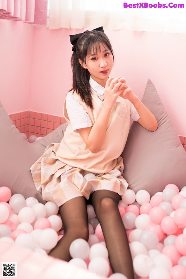 A woman sitting on top of a bed covered in pink and white balls.