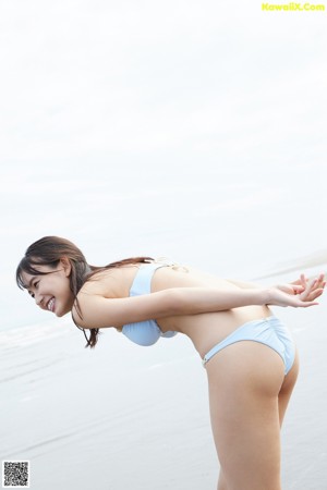 A woman in a blue bikini running on a beach.