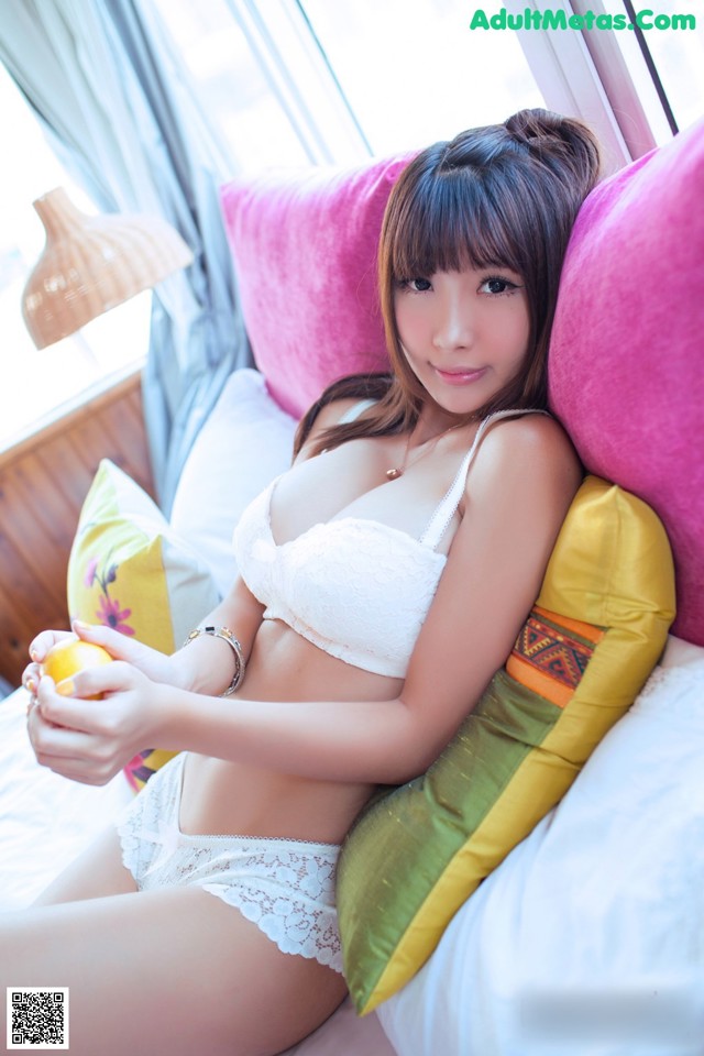 A woman in a white bra and panties sitting on a bed.