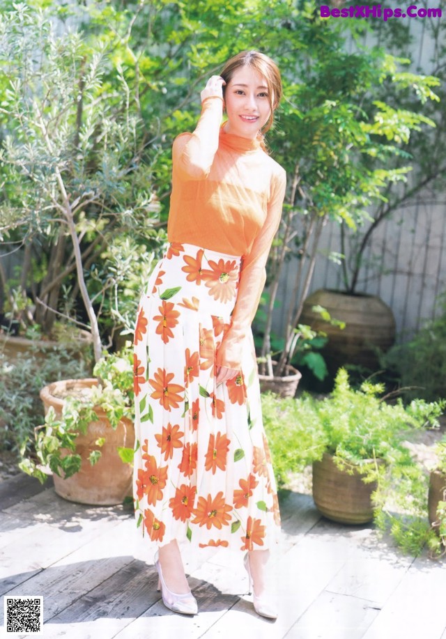 A woman in an orange top and a white skirt posing for a picture.