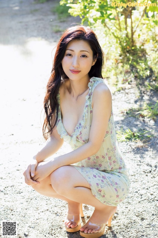 A woman in a floral dress crouching down on a dirt road.